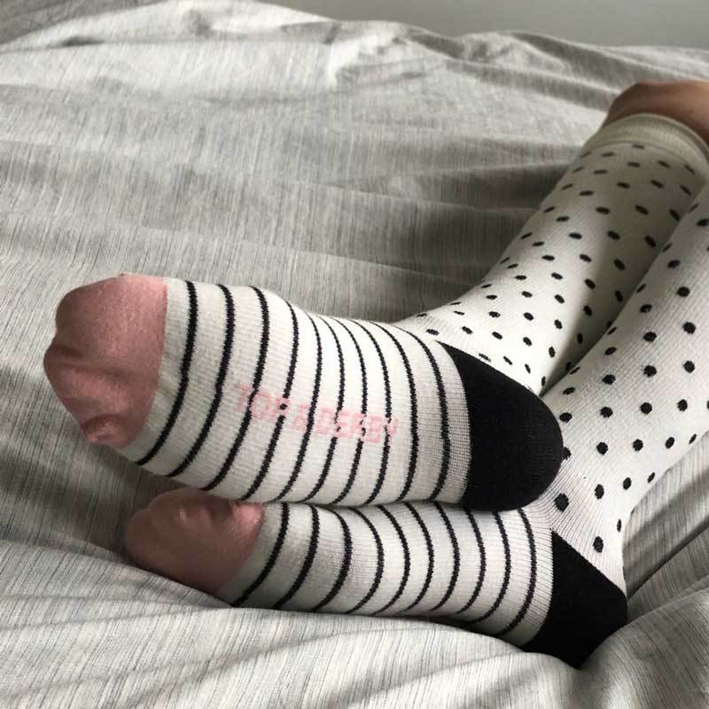 Woman's legs in bed wearing white support hose with black stripes dots and pink toes