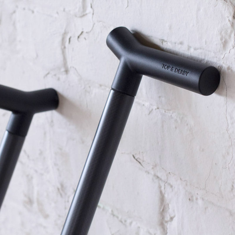 Two black CFX carbon fiber Top & Derby walking sticks leaning on brick wall