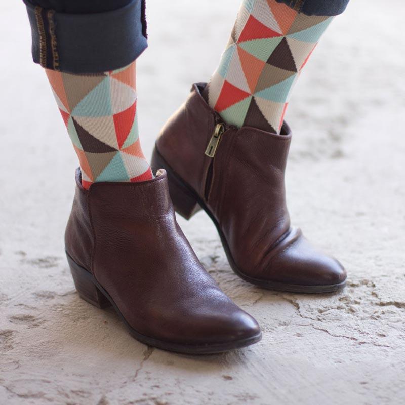 Woman's feet wearing coral cream triangle pattern energy compression socks with brown low brown boots
