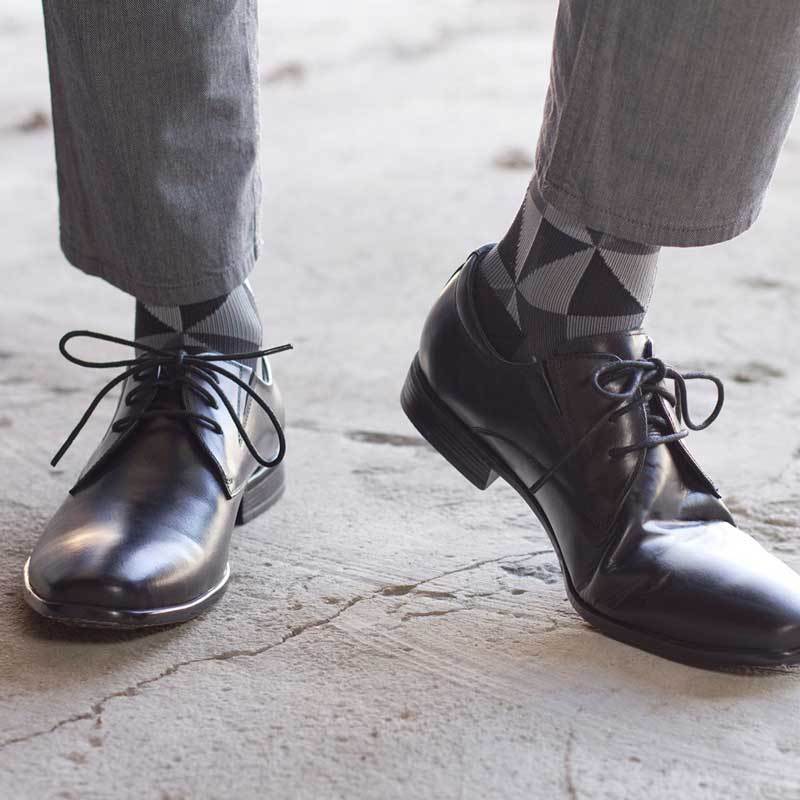 Man wearing black leather dress shoes with triangle pattern compression socks in black and grey