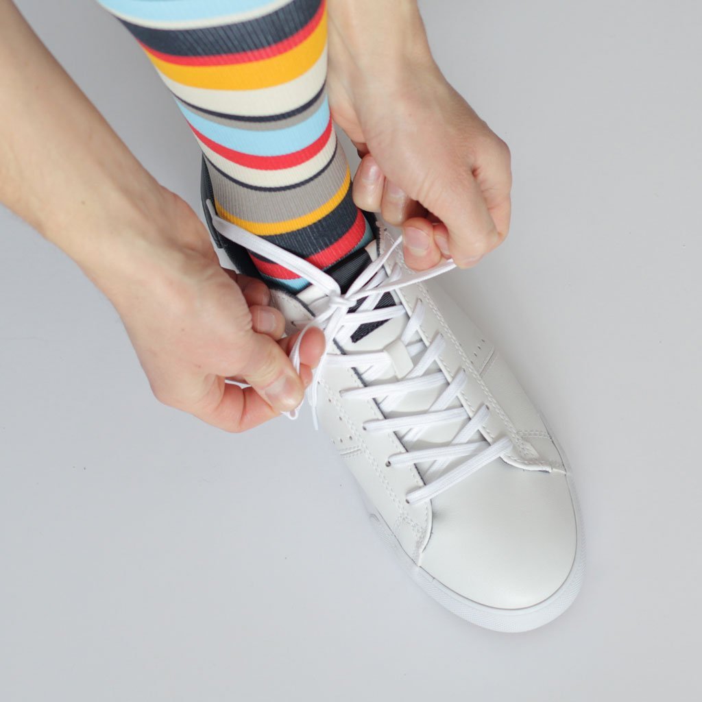 Man lacing up white sneakers wearing yellow, red and blue striped travel compression stockings